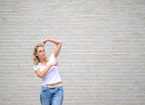 Promotional photo of an attractive friendly woman pointing to the right side in front of a white brick wall