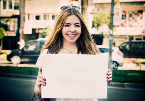 Young woman holding empty white placard in the street