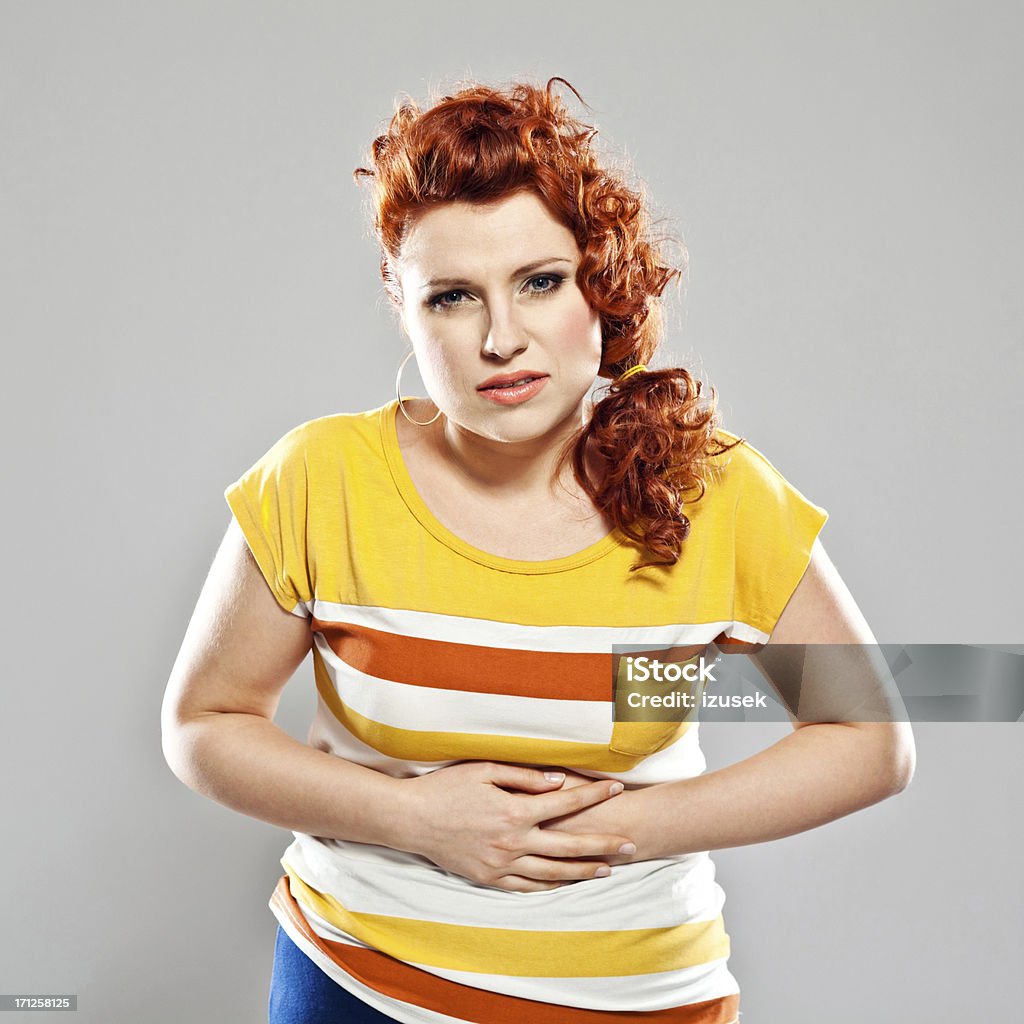 Stomach ache Portrait of young woman suffering from stomach ache. Studio shot, grey background. Menstruation Stock Photo