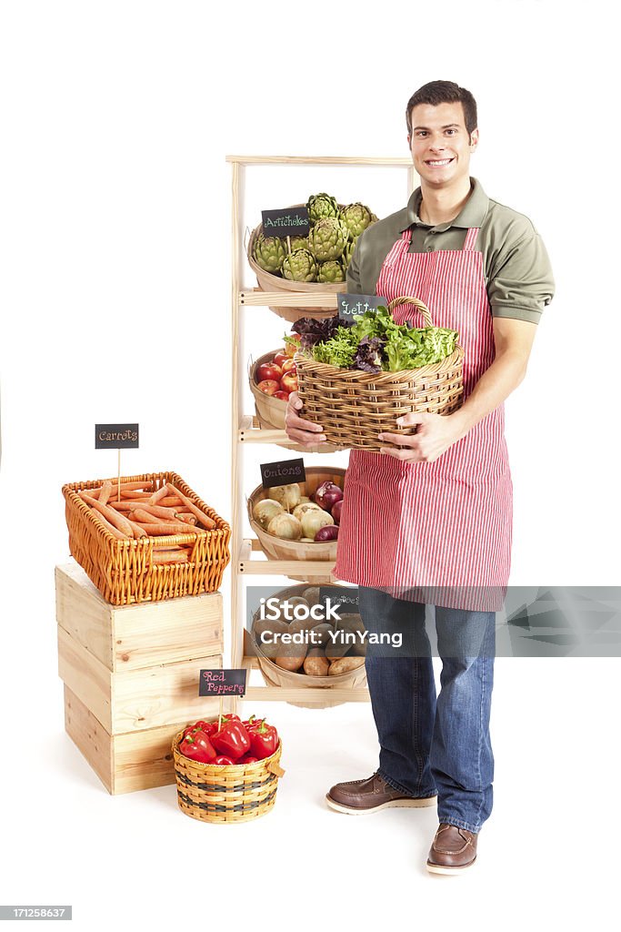 Small Business Local Grocery Store Shop Owner on White Background Subject: Smiling male grocer holding a basket of lettuce as he stands in front of a grocery retail shelf display of vegetables. Isolated on a white background. Cut Out Stock Photo