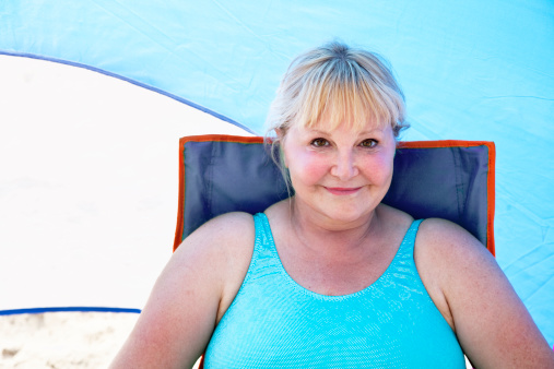 mature woman with beautiful smile wearing bathing suit, sitting in the shade on a chair in tent, enjoying vacation