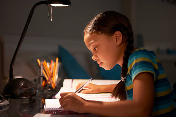 Young Girl Studying At Desk In Bedroom Young Girl Studying At Desk In Bedroom In Evening Writing Notes. desk lamp photos stock pictures, royalty-free photos & images