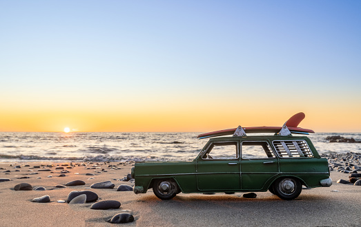 Green metal model surfing wagon at the beach water front, with a warm sunset sky.