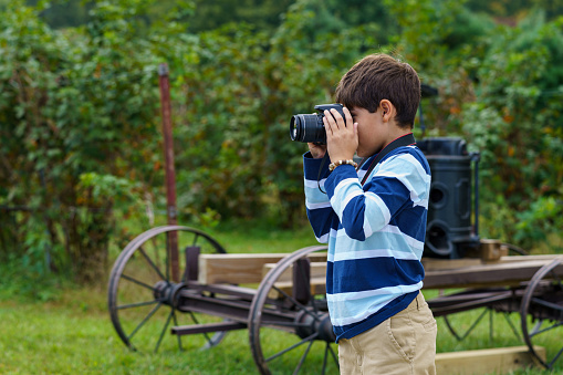 A 9 year old boy is using a DSLR digital camera outside in a farm.