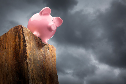 A piggy bank teetering on the edge of a cliff with stormy skies in the background.To see more of my financial images click on the link below: