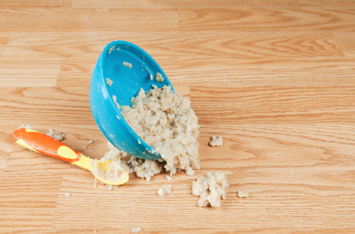 A toddler's bowl of oatmeal is falling to the floor with a spoon. This would make a good food pushed from a highchair or child frustration concept.