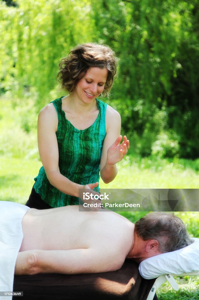 Beautiful Massage Therapist Massages Mature Man Outdoors "Mature man receiving a massage from beautiful young massage therapist in vibrant green outdoor setting.Shot with Canon 5D2, processed with slight color saturation added.  Some possible motion blur on hands." 20-29 Years Stock Photo