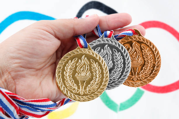 Three medals with Olympic Flag "Cantley, Canada - Mai 8, 2012: Three Generic medals with sport torches in hand with in the background a part of Olympic Flag in the wind which is composed of five interlocking rings in blue, yellow, black, green and red." 2012 stock pictures, royalty-free photos & images