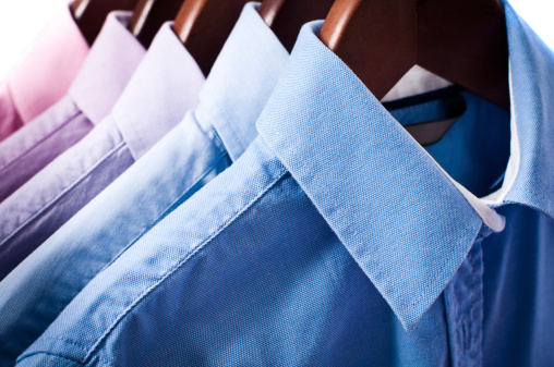 Close-up of blue and pink elegant button down shirts are hanging on wooden hangers.