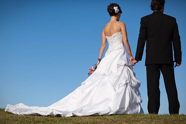 Color image of the rear view of a happy bride and groom, standing outdoors on summer day.