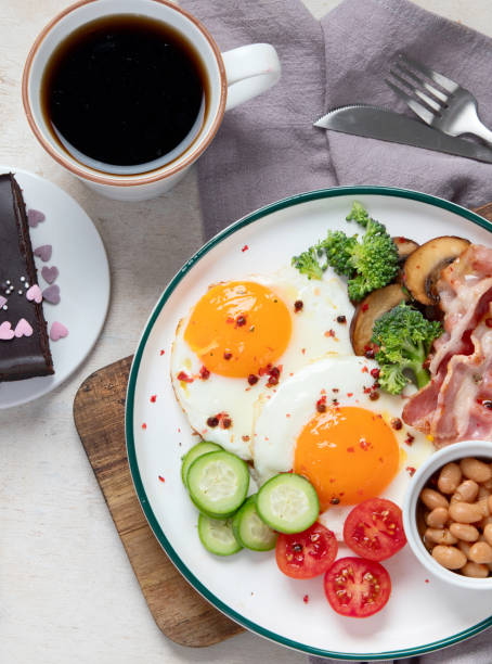 traditional englis breakfast plate with bacon strips, sunny side up eggs, vegetables and cake on light background - englis imagens e fotografias de stock