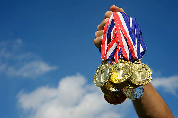 Athlete Hand Holding Up Bunch of Gold Medals Blue Sky Hand holds up a bunch of gold, silver, and bronze medals in bright blue sky gold medal stock pictures, royalty-free photos & images
