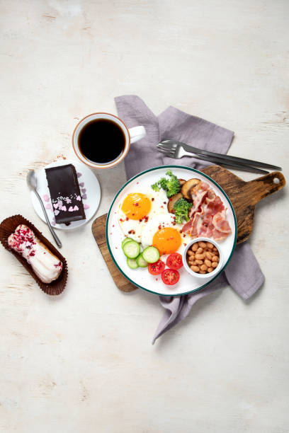 traditional englis breakfast plate with bacon strips, sunny side up eggs, vegetables and cake on light background - englis imagens e fotografias de stock