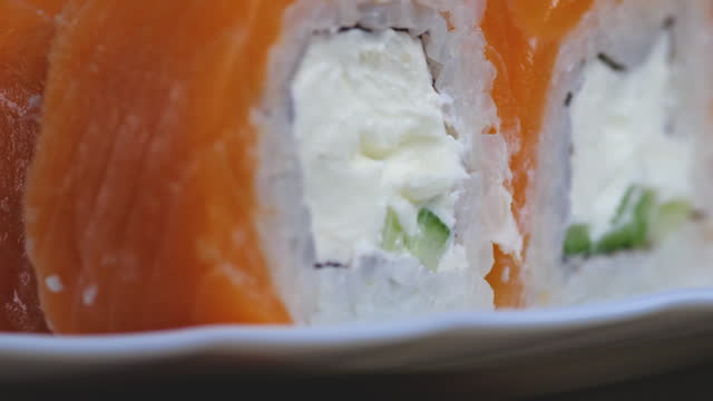 extreme close-up set of sushi with rice, salmon, cheese sauce, cucumber on a plate rotation. appetizing sushi macro. Japanese cuisine restaurant. food delivery