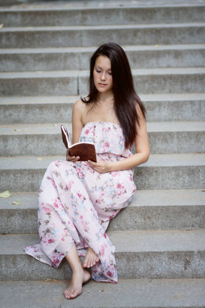 Young woman reading a book sitting on the bench on the beach at sunset.