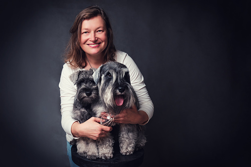 Smiling woman with two miniature schnauzer dogs on black background