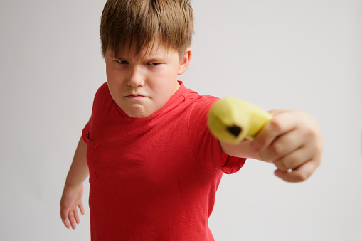 Child boy playing with a yellow banana on a gray background