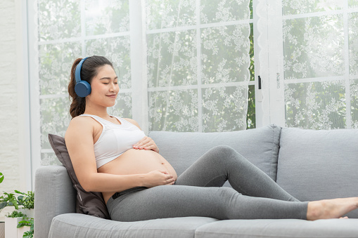 Young Attractive Asian pregnant woman listen music and lying on bed.Pregnant woman use headphones to play classical music for baby in belly learn and Development feeling so relax,Pregnancy Concept