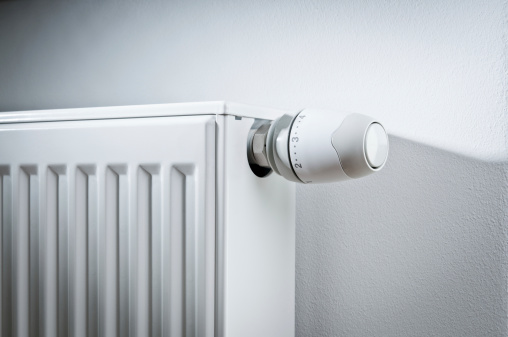 Close-up of modern white radiator with thermostat reduced to economy mode.