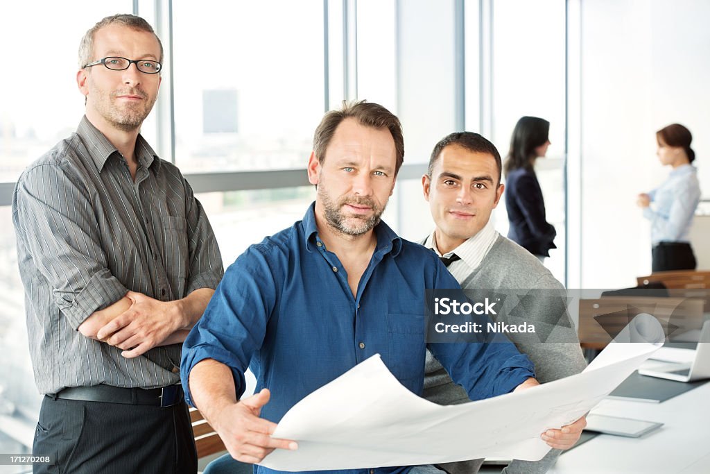Engineers With Blueprint Portrait of confident male engineers reviewing blueprint with female colleagues standing in background. Horizontal shot. 30-39 Years Stock Photo