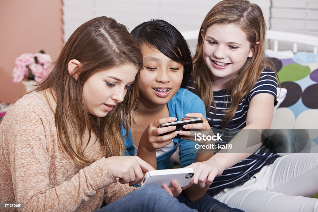 Girls texting Multi-ethnic preteen girls (12 years) with mobile phones, texting.  Focus on Asian girl. Pre-Adolescent Child Stock Photo