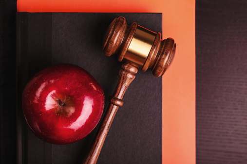A gavel and an apple on a desk with books.