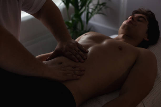 doctor therapist doing wellness abs body massage for sporty male, hands massaging belly indoors in shadow. handsome athletic man visit masseur in medic room. rehab massage concept. copy ad text space - massage therapist massaging sport beautician imagens e fotografias de stock
