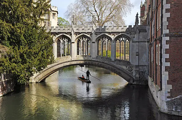 "A punt  beneath The Bridge of Sighs, St John's College, Cambridge UniversityEarly morning light casts atmospheric shadows and reflectionsEngland, UKThe Bridge of Sighs in Cambridge is a covered bridge belonging to St John's College of Cambridge University. It was built in 1831 and crosses the River Cam between the college's Third Court and New Court."