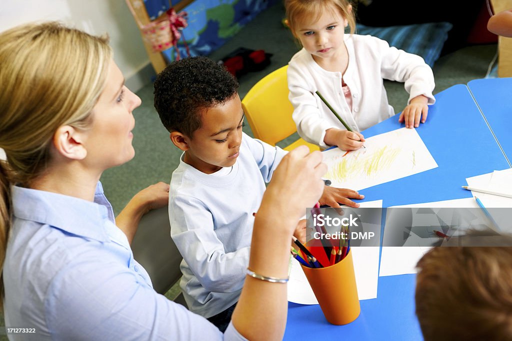 Helpful young teacher with preschoolers in class room Helpful young teacher with preschoolers in class room at kindergarten Activity Stock Photo