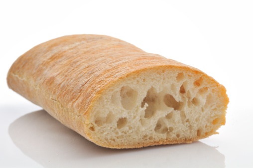 Italian ciabatta bread cut in half isolated on a white background with a reflection in the foreground.