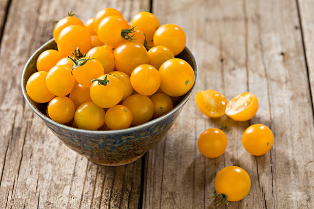 Yellow Sungold Cherry Tomatoes A high angle close up shot of a bluish bowl overflowing with freshly harvested sungold yellow cherry tomatoes. Shot on a grungy old outdoors table. cherry tomato stock pictures, royalty-free photos & images