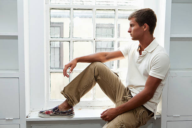 Contemplative teenage boy sitting next to window