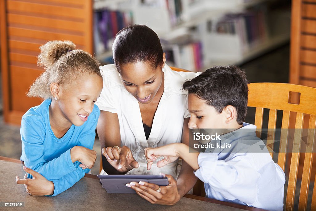 Niños con profesor utilizando tableta digital en biblioteca - Foto de stock de 20 a 29 años libre de derechos