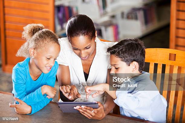 Niños Con Profesor Utilizando Tableta Digital En Biblioteca Foto de stock y más banco de imágenes de 20 a 29 años