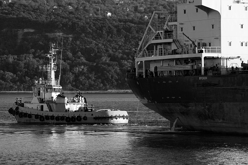Tug boat is near a cargo ship. Black sea, Varna harbor, Bulgaria. Black and white photo