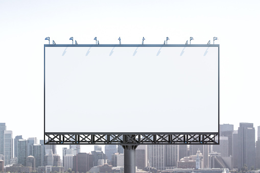 Blank white billboard on city buildings background at daytime, front view. Mockup, advertising concept