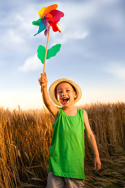 Happy little boy holding colorful pinwheel standing on the wheat field.