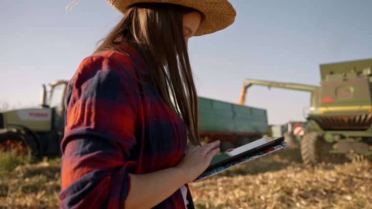 SLO MO Young Female Farmer Using Digital Table while Watching Combine Unloading Corn Grains into Tractor at Field