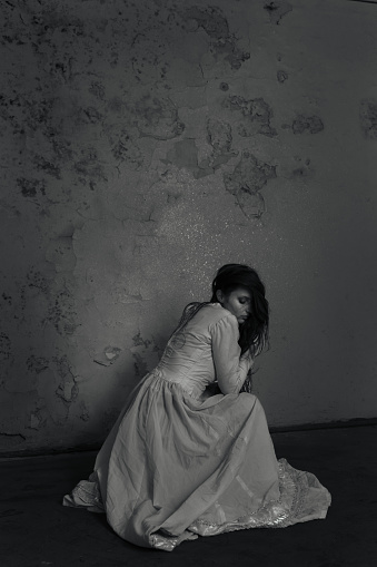 Careless young woman sitting barefoot in an empty room, full of mold and dirt.