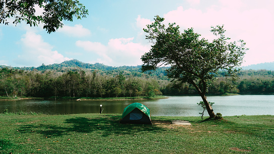 Tent on field against lake. Landscape shot of sunset at a beautiful lake in Thailand. Camping green tent in forest near lake.
