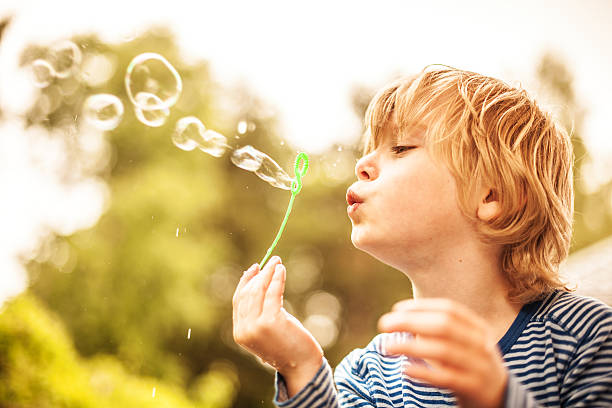linda poco niño soplando burbujas de aire libre - bubble child bubble wand blowing fotografías e imágenes de stock
