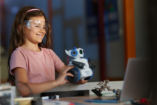 Happy elementary schoolgirl learning about futuristic robot in laboratory.