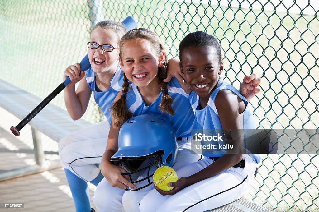 Girls softball team sitting in dugout Multi-ethnic girls (9 years) on softball team at the ball park, sitting in dugout. Child Stock Photo