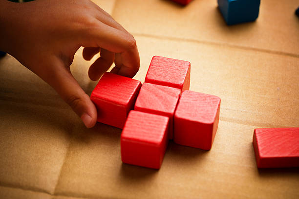 Close up of a child hand making a cross shape using red wood blocks on a cardboard surface. Conceptual picture about charity and children.Related picture:
