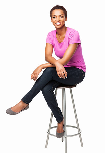 Smiling African American Woman Sitting On Chair - Isolated Full length portrait of a casual smiling African American woman sitting on chair. Vertical shot. Isolated on white. legs crossed at knee stock pictures, royalty-free photos & images