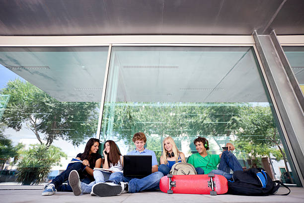teenager after school happy fifteen years old teenager group together sitting on the floor outside of the school in front of a glass door with the reflection of the urban scene secondary school activities stock pictures, royalty-free photos & images