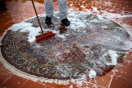 Man washing a rugs on the tile floor.