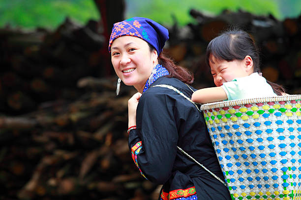 Yang Di village, Yangshuo, Guangxi, China - March 29, 2010: On country road in farmland is walking asian family, women and children, farmer carries on his shoulder a pole counterbalance to two baskets