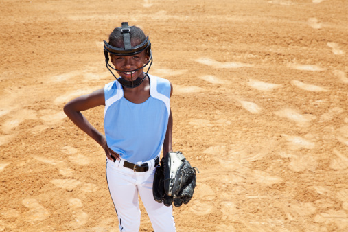 African American girl (9 years) playing softball, wearing face mask (standard safety gear required in many leagues).