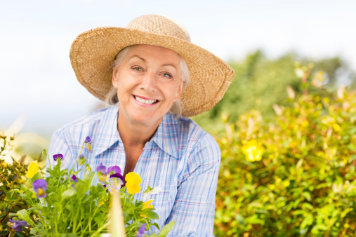 Portrait of happy senior woman wearing straw hat in garden. Horizontal shot.
